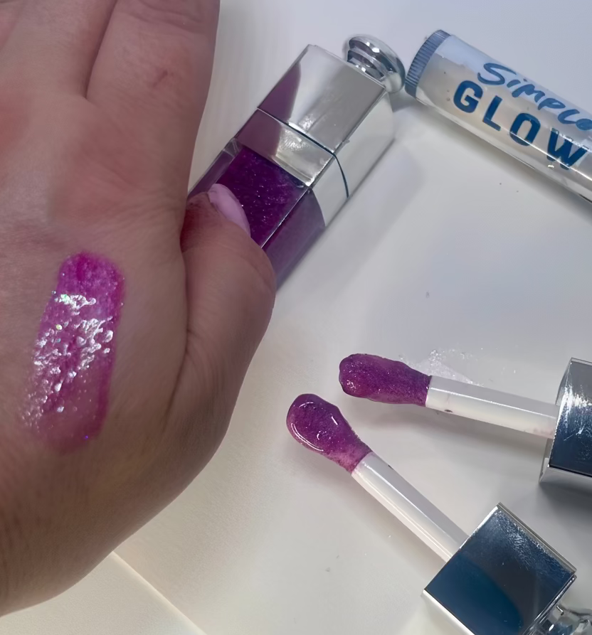 Hand with mauve glittery lip gloss swatch and lip gloss applicators on a white background