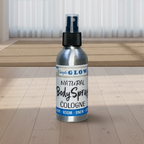 A silver bottle of Glow Natural Body Spray Cologne stands on a light wood floor in a bright, modern room with sheer white curtains and a woven rug.