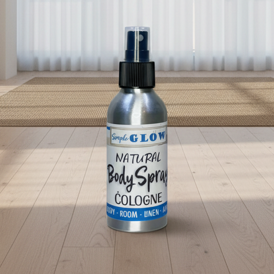 A silver bottle of Glow Natural Body Spray Cologne stands on a light wood floor in a bright, modern room with sheer white curtains and a woven rug.