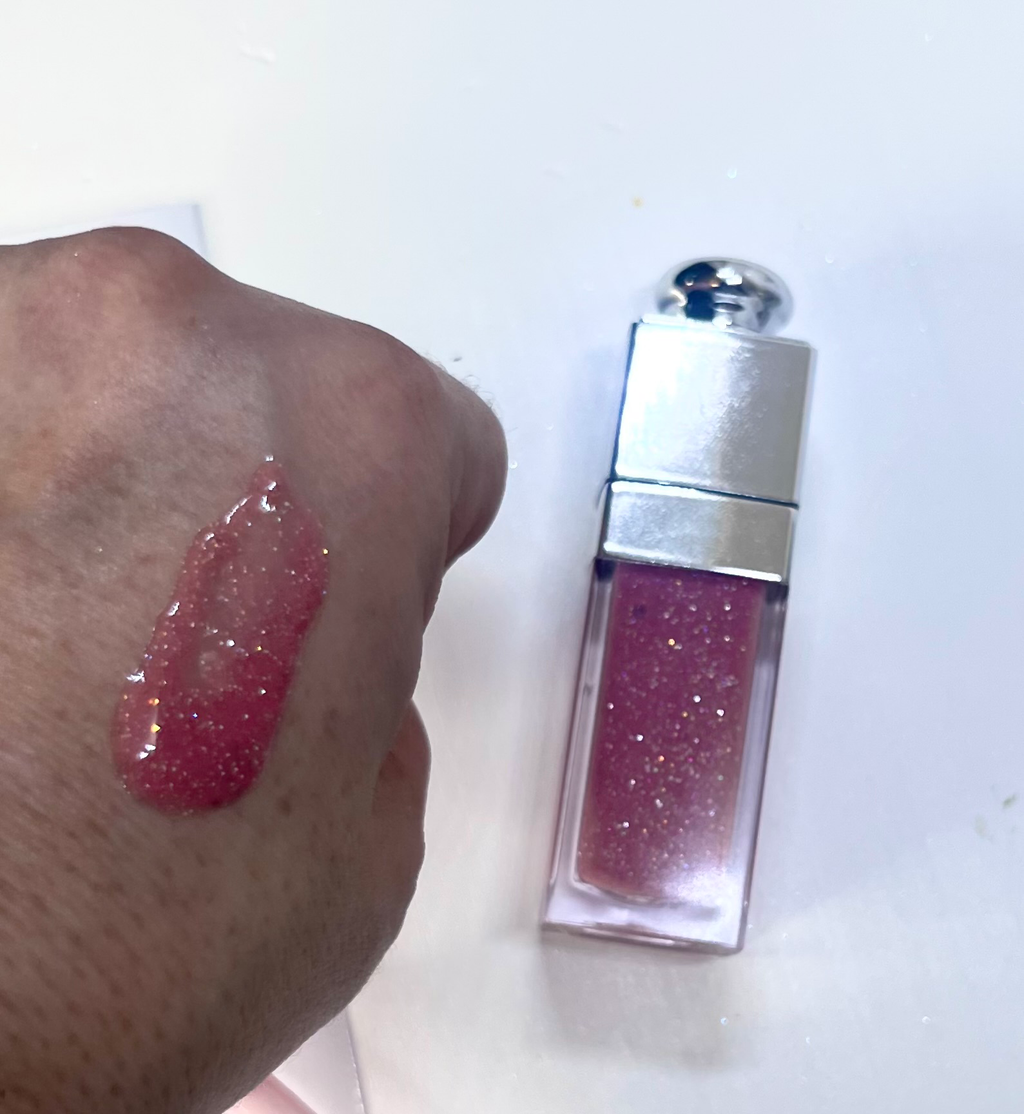 Pink glittery lip gloss applied to a hand with a white background