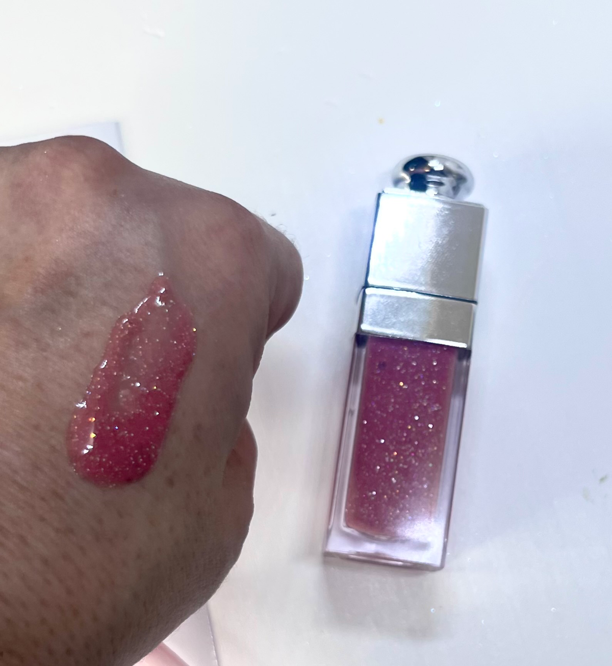 Pink glittery lip gloss applied to a hand with a white background